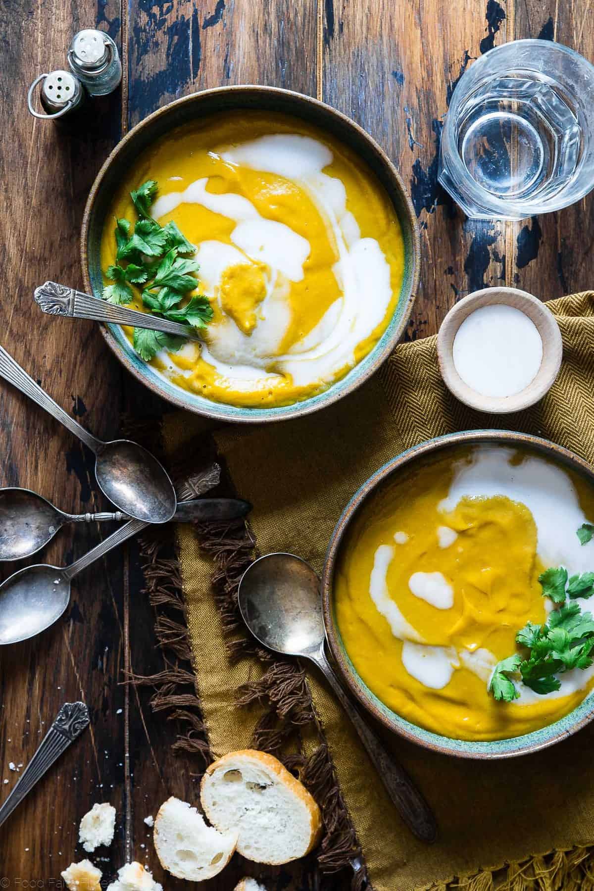 two bowls of paleo butternut squash soup on a table with spoons around