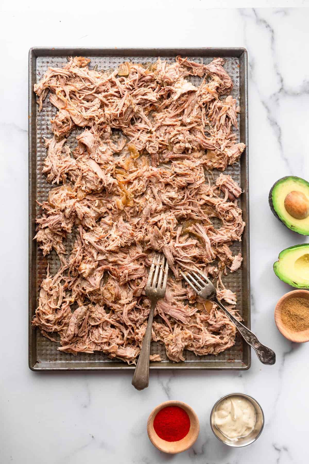 keto pulled pork being shredded with forks on a cutting board