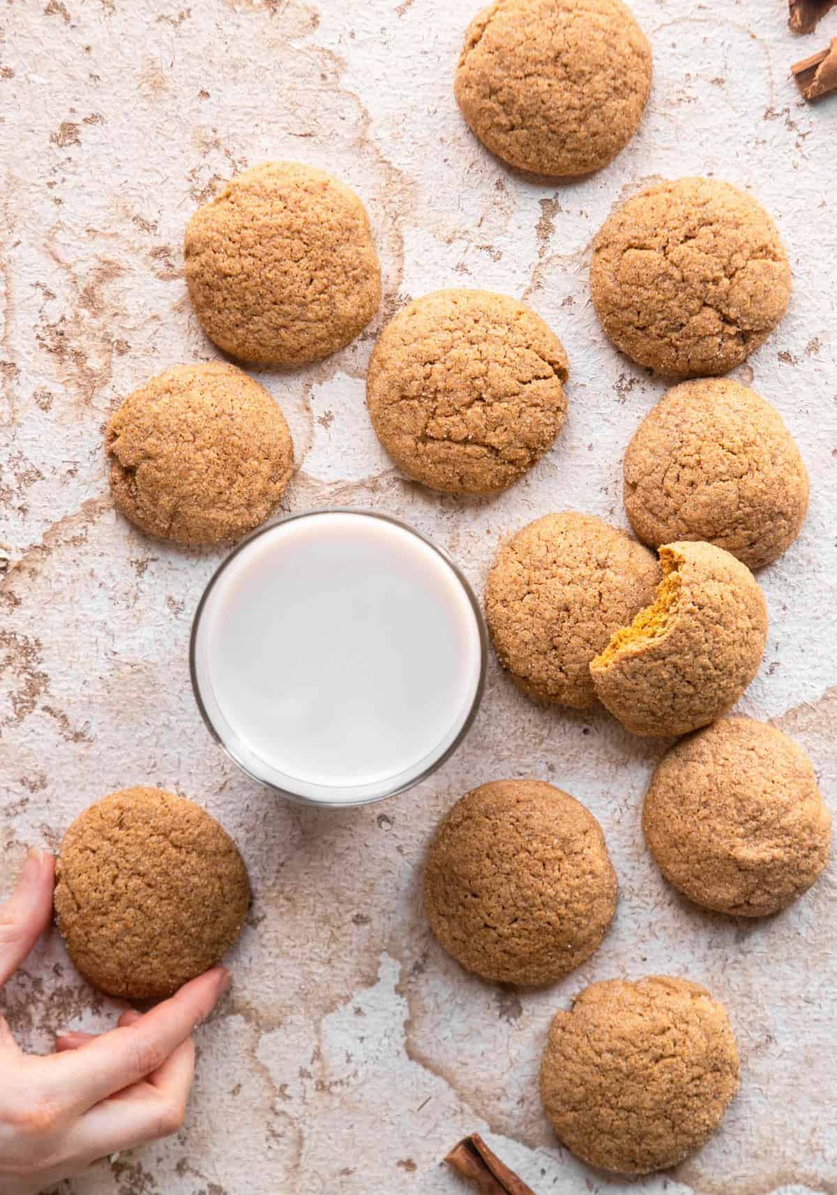 pumpkin sugar cookies on a counter with a glass of milk on the side