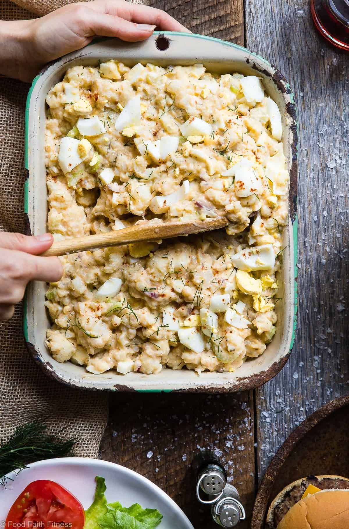 Cauliflower Potato Salad being scooped out of serving dish with wooden spoon