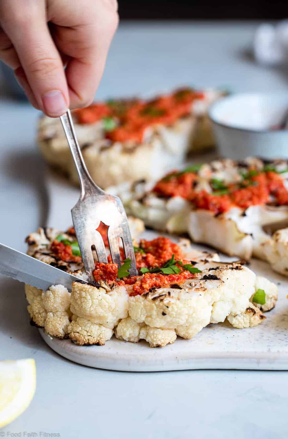 A fork and knife cutting into roasted cauliflower steak