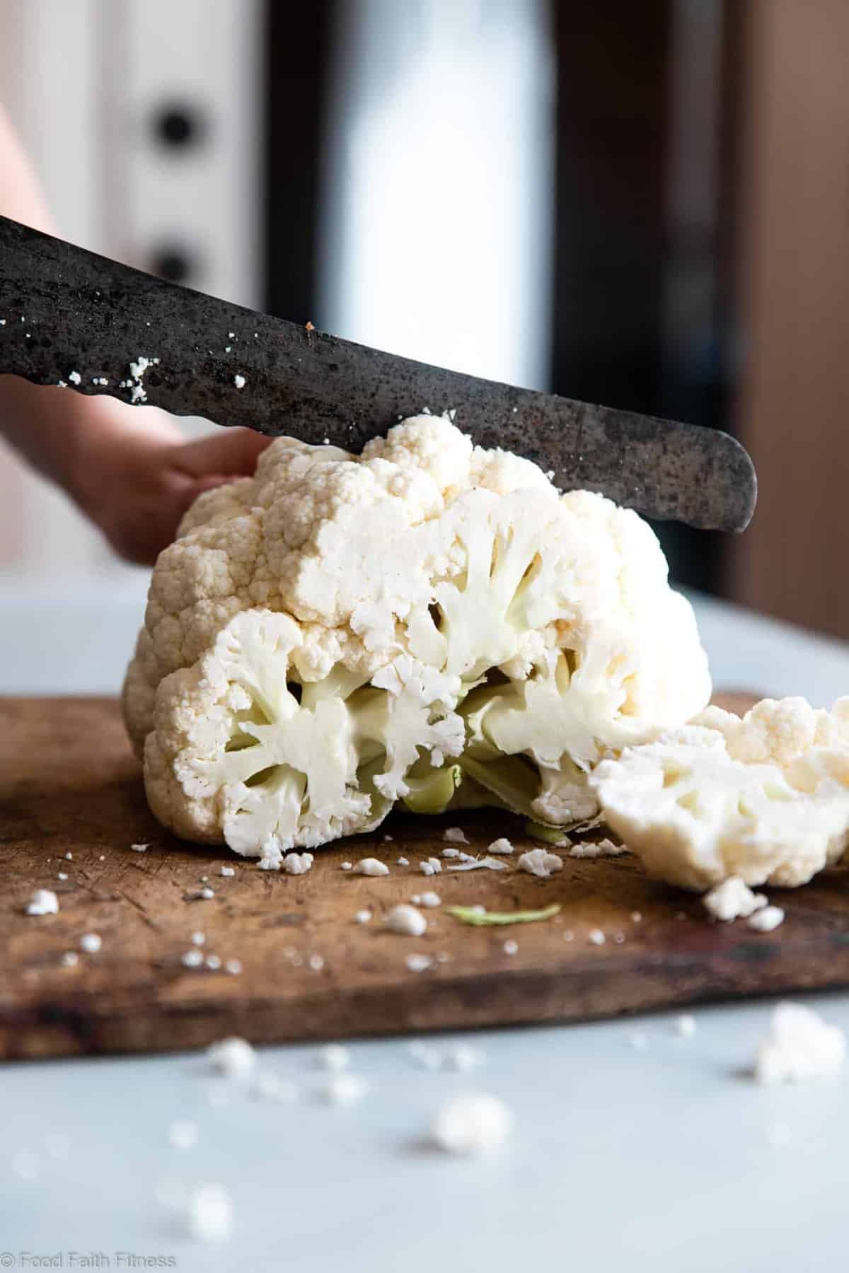 A hand slicing a head of cauliflower for a cauliflower steak recipe