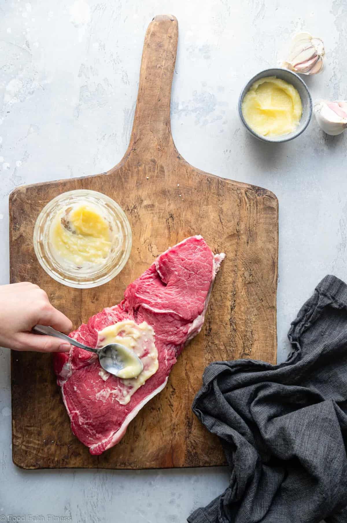 spreading butter onto raw steak on a cutting board