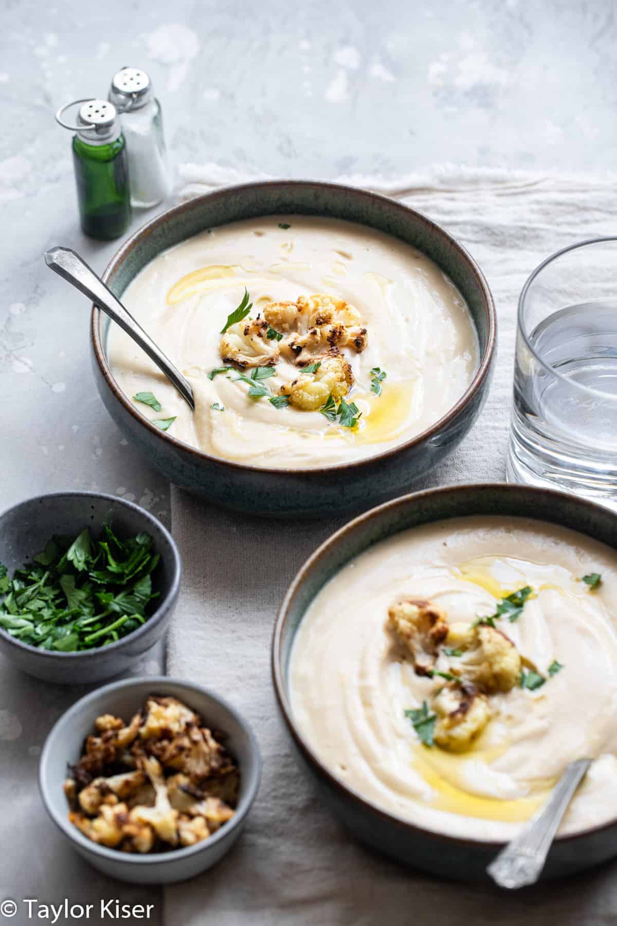 two bowls of keto cauliflower soup with spoons in them