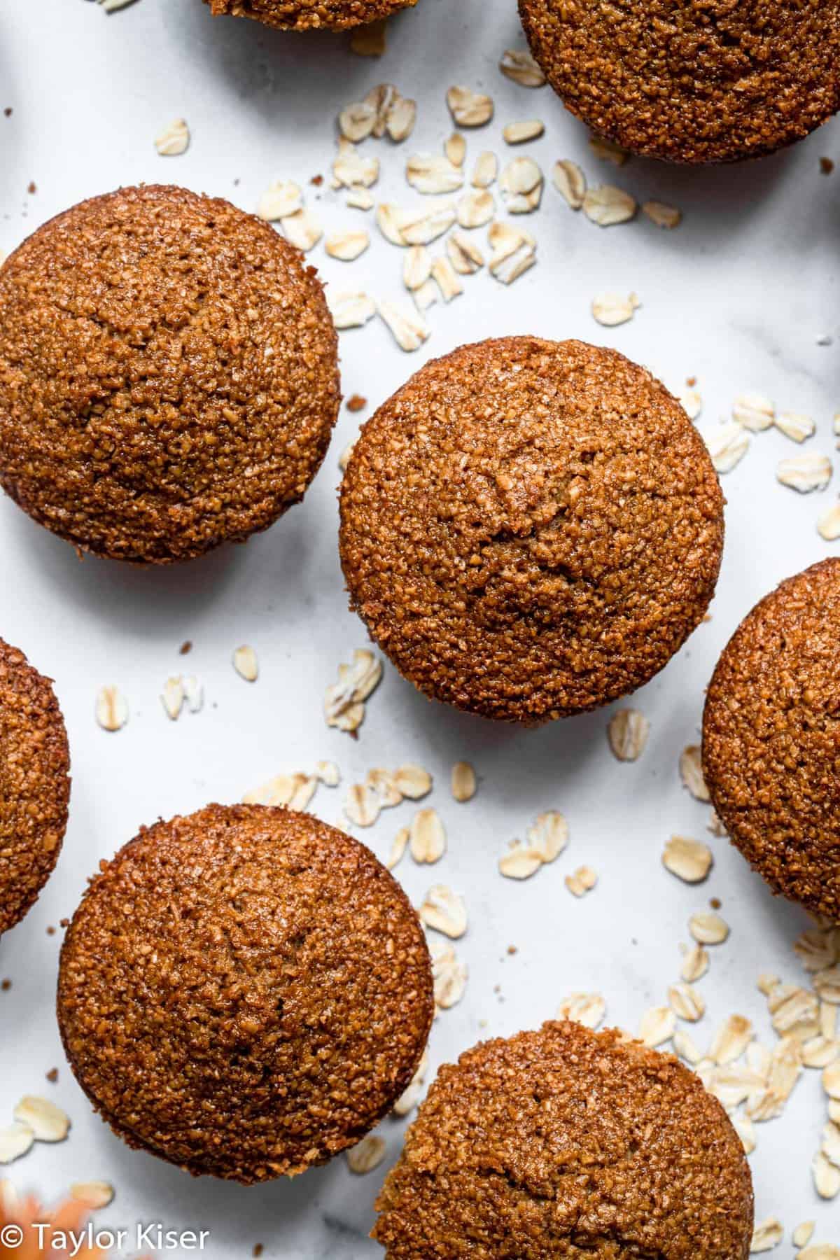 the tops of healthy oat bran muffins on a table with oats around them