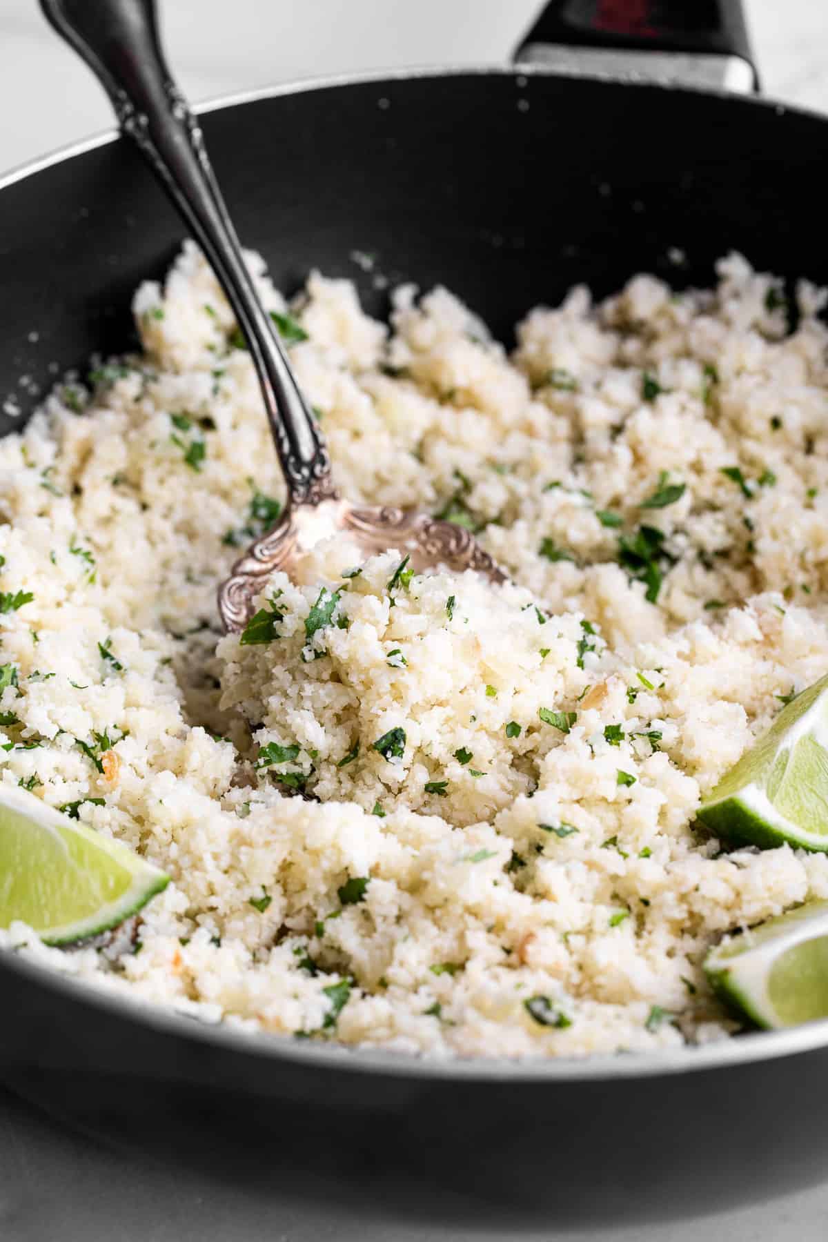 cilantro cauliflower rice in a skillet with limes