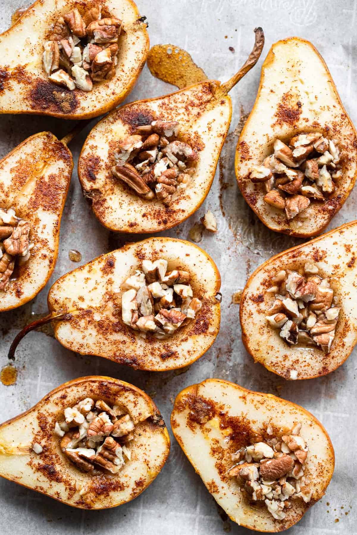 close up of whole baked pears on a cookie sheet with pecans
