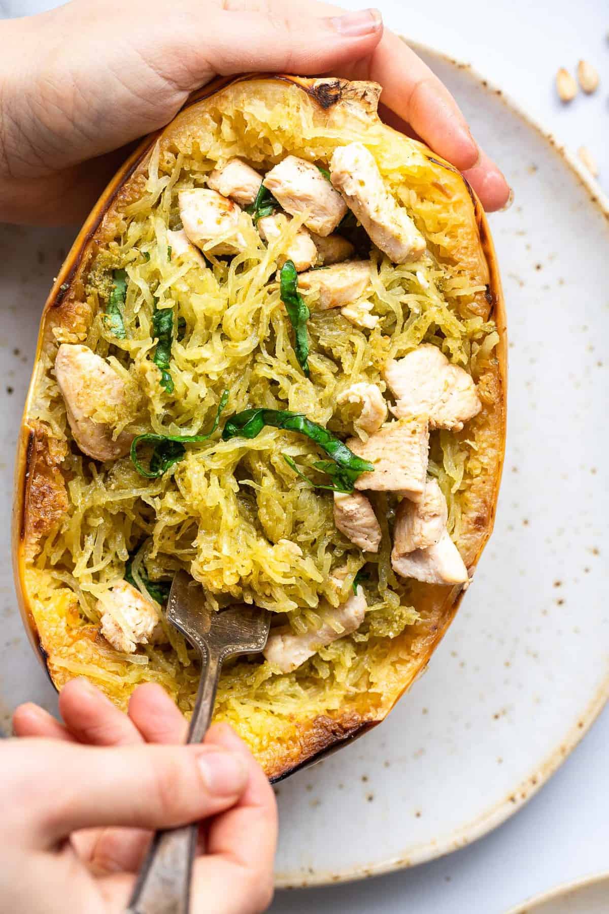 a hand holding chicken pesto spaghetti squash and digging a fork in