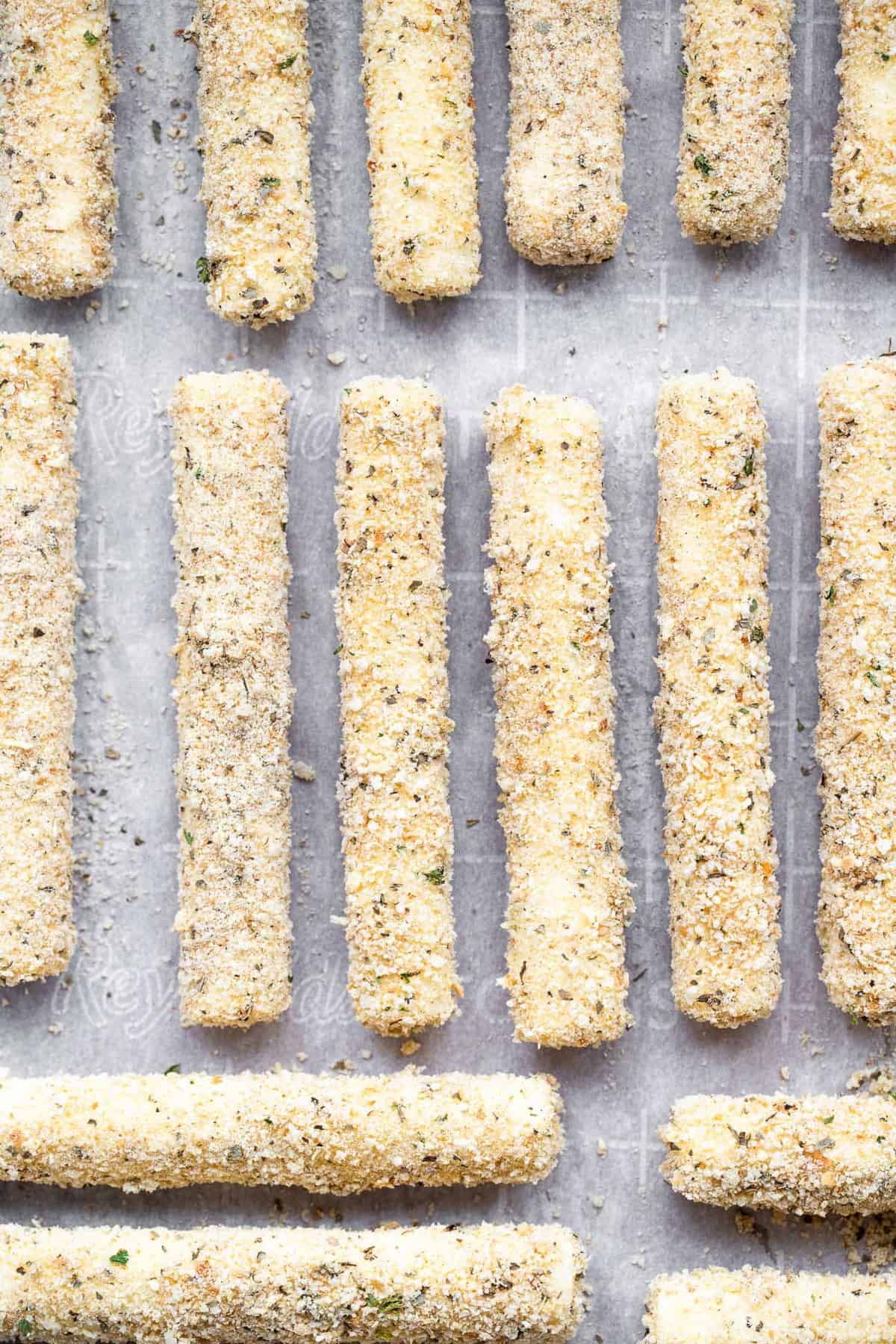 baked cheese sticks lined up on a baking sheet