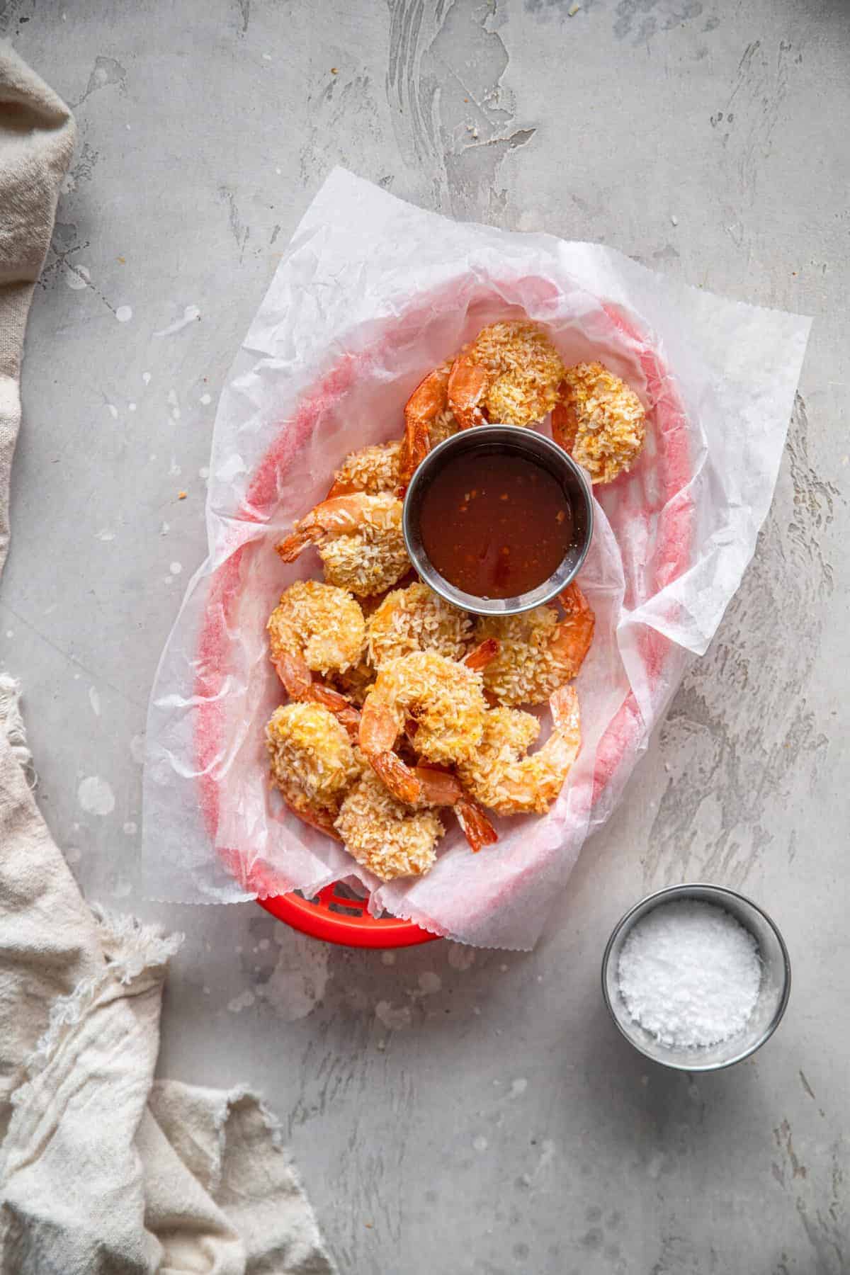 Air fryer fried shrimp in a basket with sauce and coconut flakes