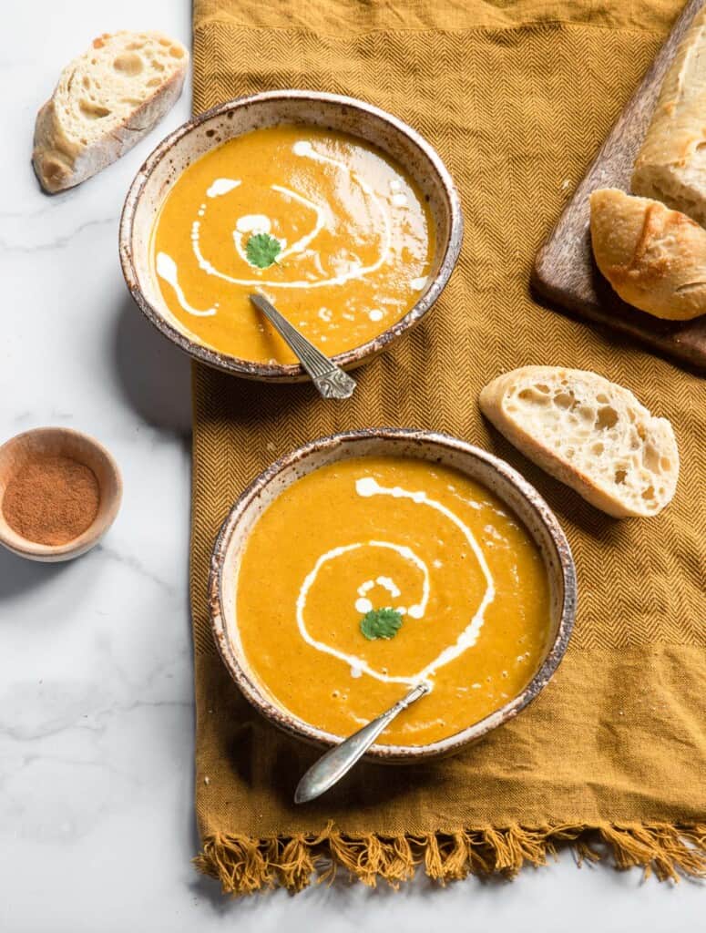 two bowls of Instant Pot Butternut Squash Soup with bread and seasoning on the side