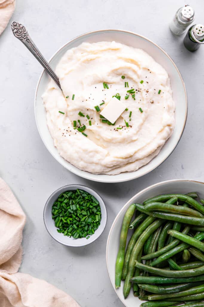 Instant Pot Mashed Cauliflower in a serving bowl with green beans on the side