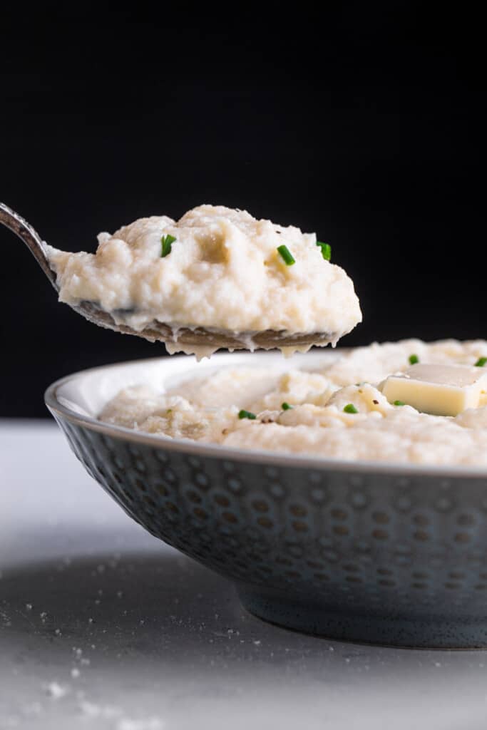 side view of Instant Pot Mashed Cauliflower in a bowl being scooped with a spoon