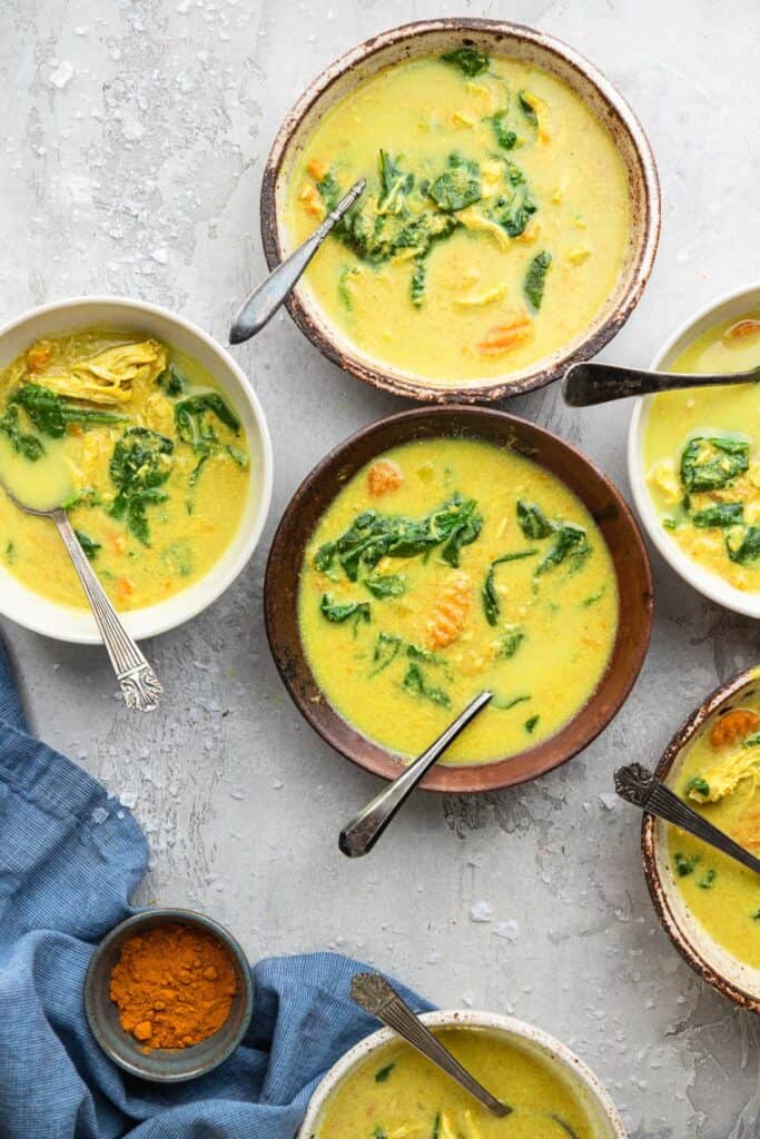 various bowls of Whole30 Instant Pot Turmeric Tahini Chicken Soup on a table with spoons