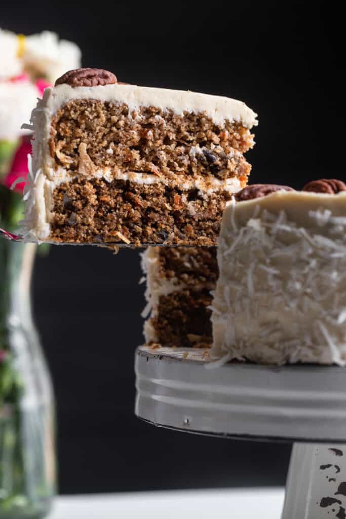 Low Carb Keto Carrot Cake on a cake stand with a piece being lifted out