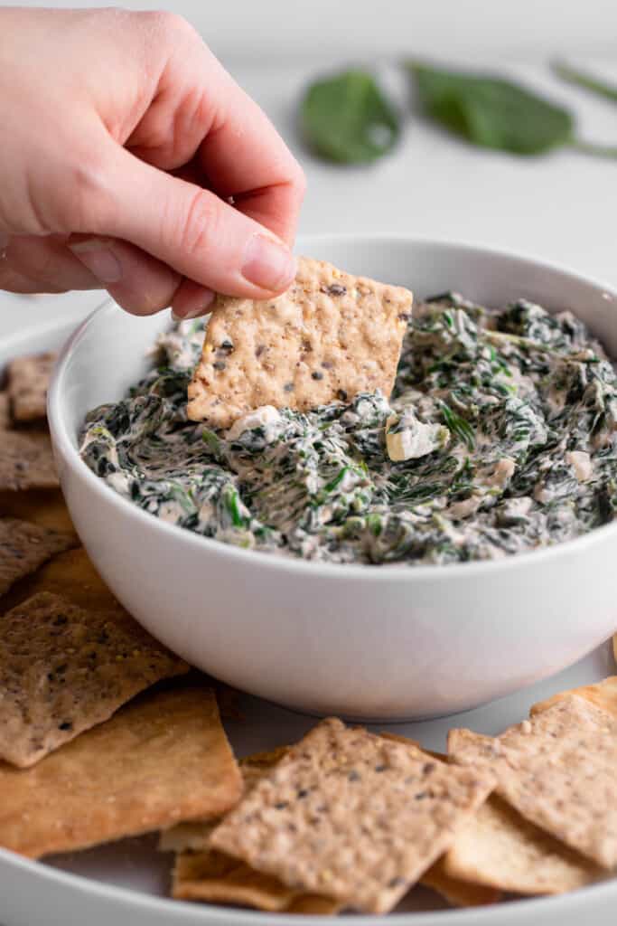 a cracker being dipped into Vegan Spinach Dip