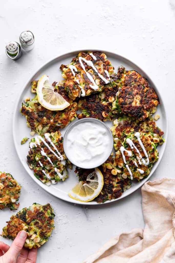 a large serving plate with Zucchini Corn Fritters and sour crem