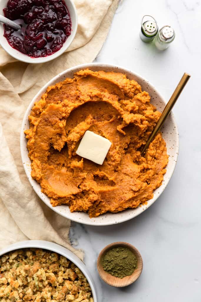 a serving bowl of Healthy Mashed Sweet Potatoes on a table with sides