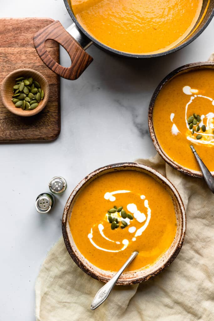 tow bowls of Pumpkin Bisque on a table with toppings on the side