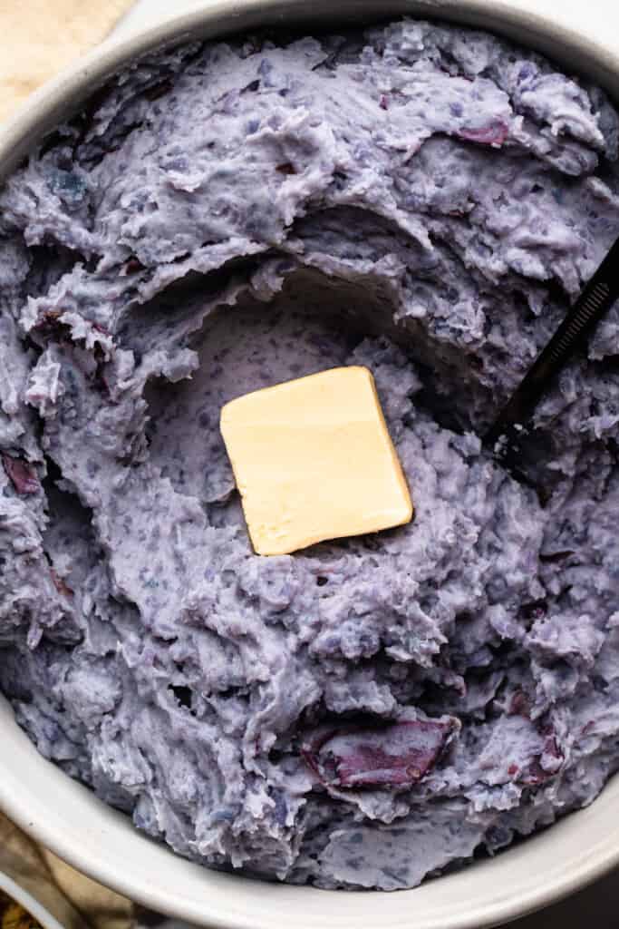 a bowl full of Purple Mashed Potatoes with butter on top