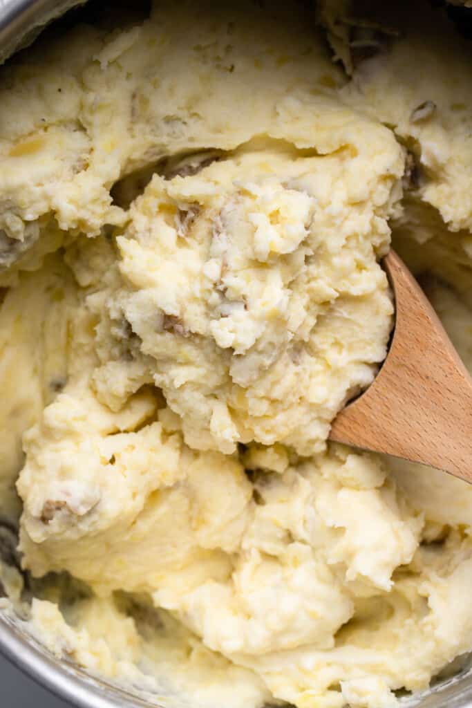 a wooden spoon in a pot of Healthy Mashed Potatoes