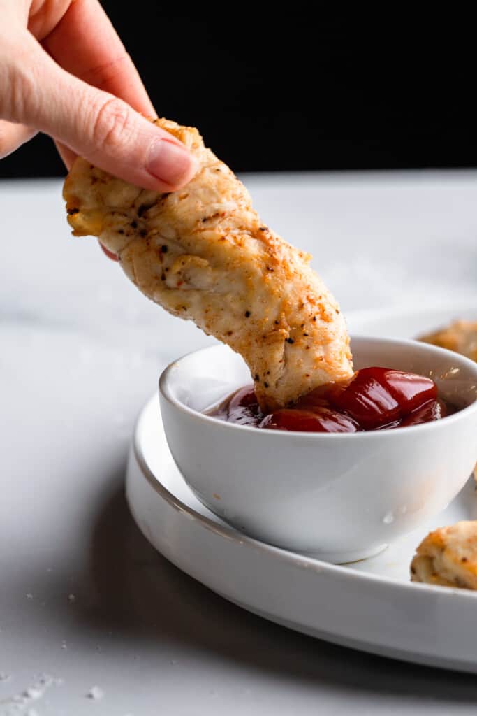 Air Fryer Chicken Tenders No Breading being dipped into sauce