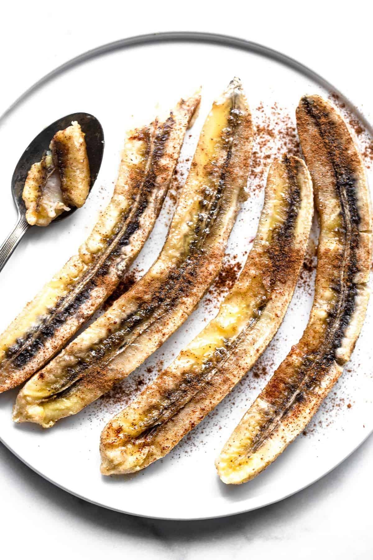4 baked bananas on a plate with cinnamon on top